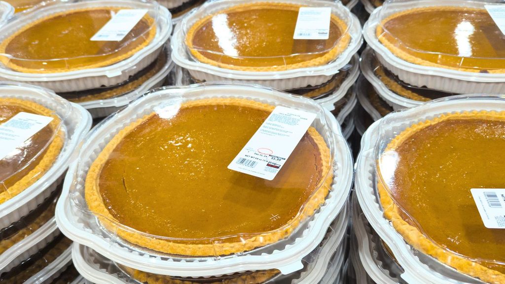Stacked pumpkin pies for Halloween shopping, housed in clear plastic containers with price and ingredient labels.