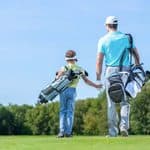 A man and a young child, both carrying golf bags, walk across a golf course.