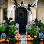 A house entrance decorated for Halloween with spiderwebs, large fake spiders, tombstones, and pumpkins.