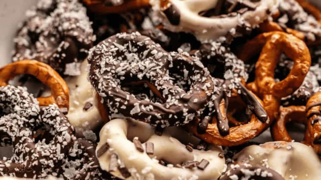 A variety of pretzels coated in dark and white chocolate, some topped with coconut shavings or chocolate sprinkles.