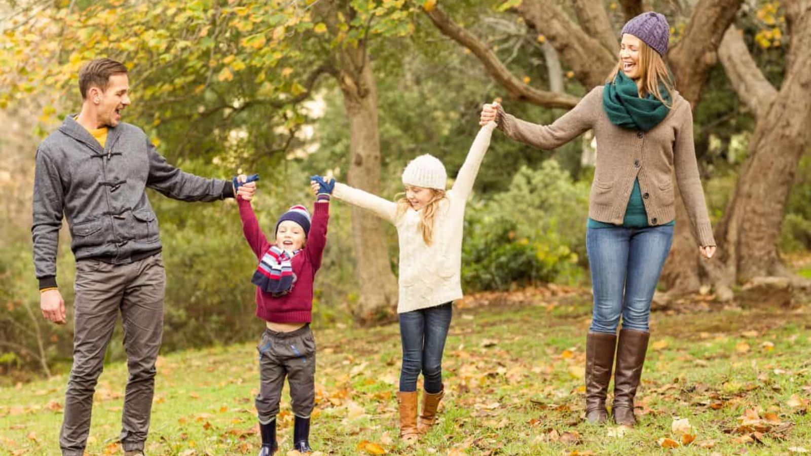 A family of four holding hands and walking through a park in autumn.