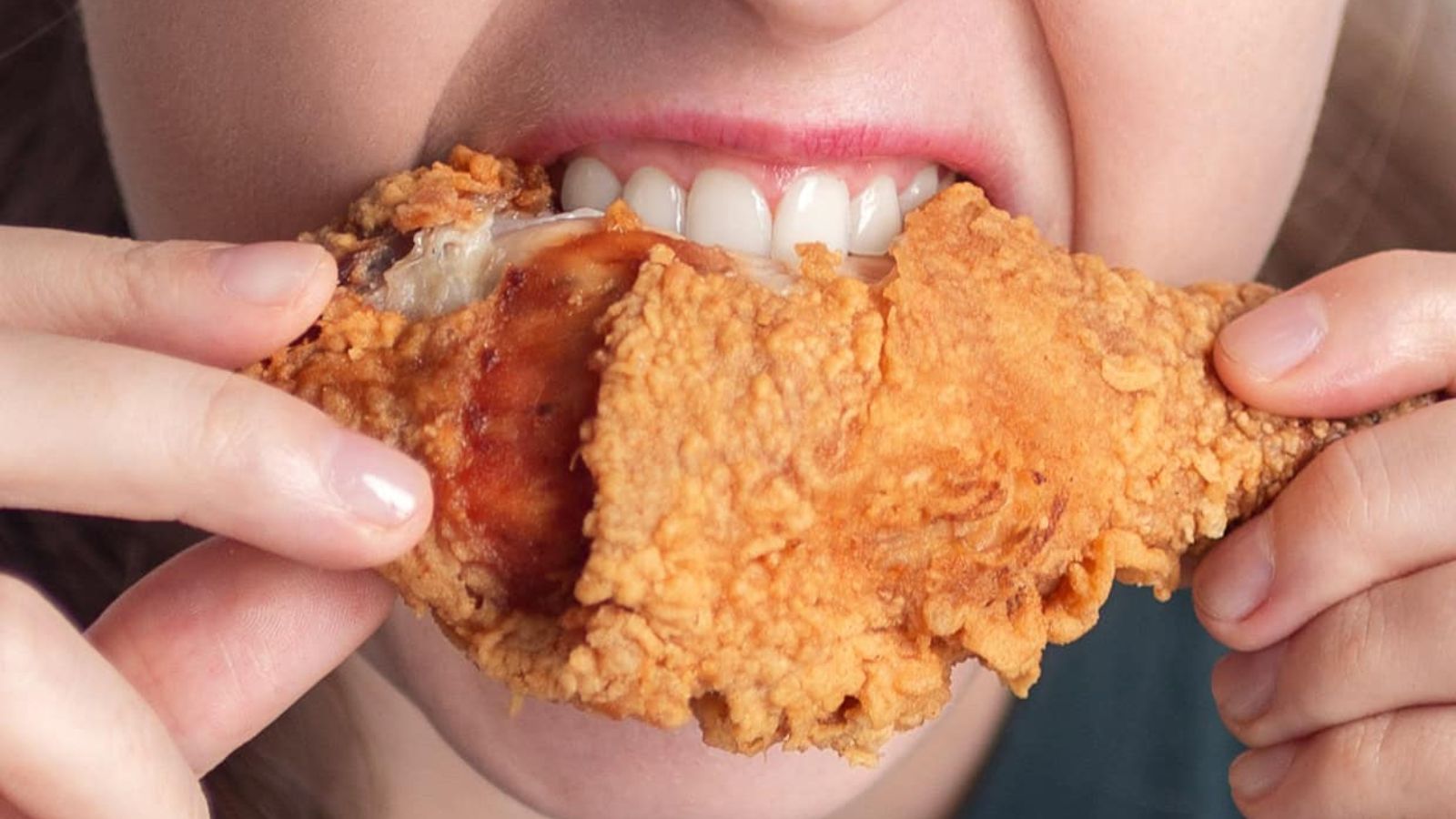 A person biting into a piece of crispy fried chicken.