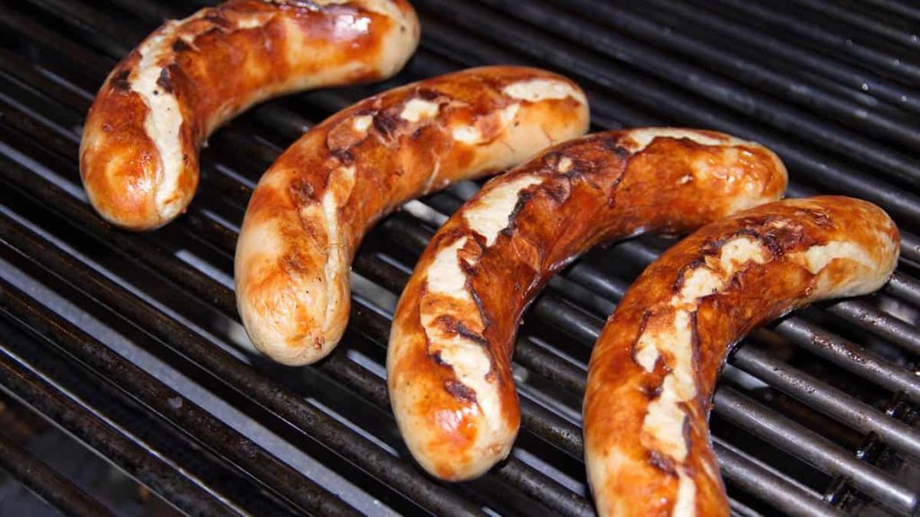 Four browned sausages grilling on a metal grate.