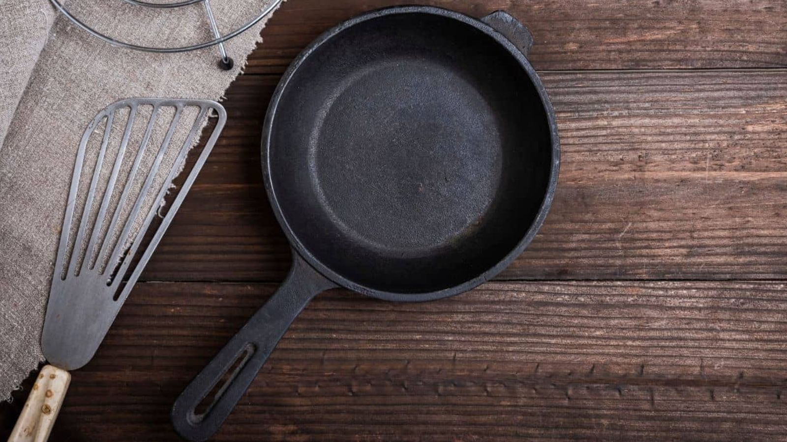 An empty cast iron skillet sits next to a metal spatula on a wooden surface, perfect for following expert cast iron advice.