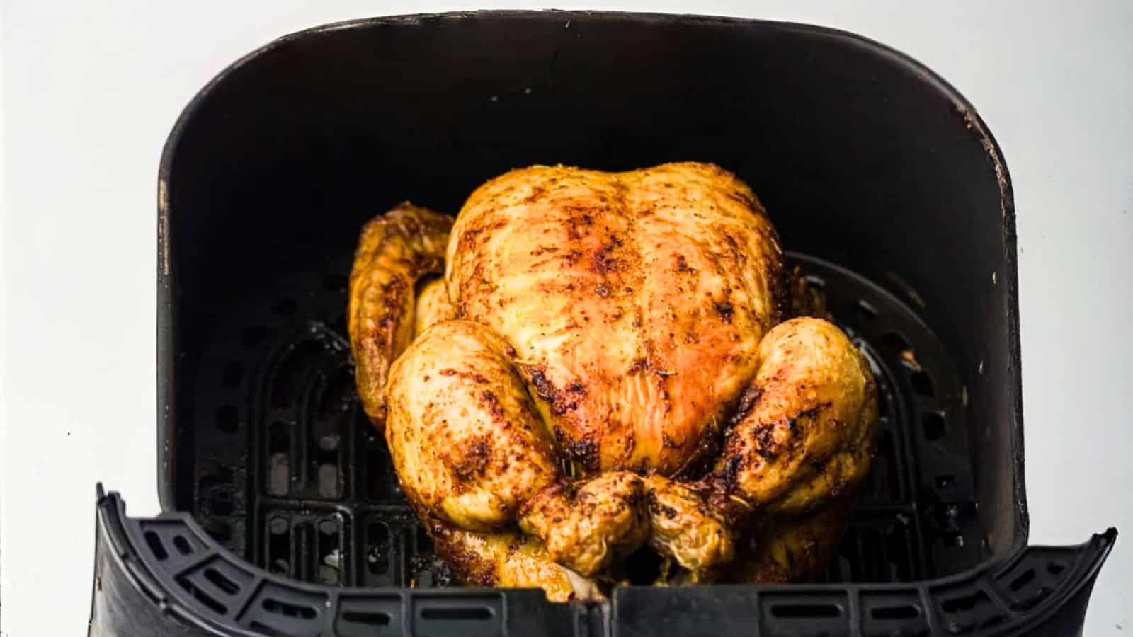 A whole roasted chicken inside an air fryer basket.