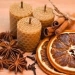 Three honeycomb pillar candles surrounded by star anise, cloves, cinnamon sticks, and dried orange slices.