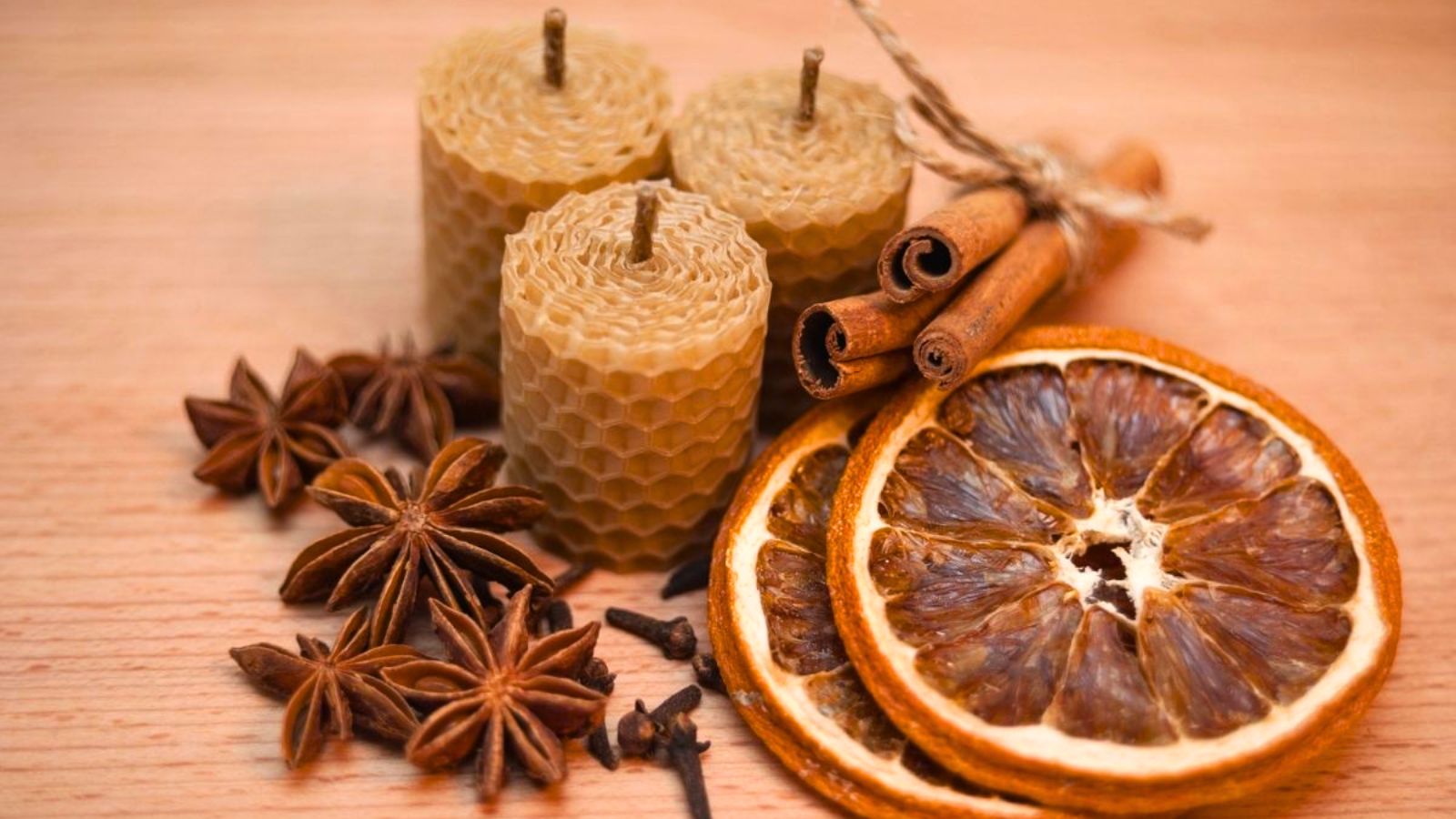 Three honeycomb pillar candles surrounded by star anise, cloves, cinnamon sticks, and dried orange slices.