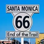 Route 66 sign in Santa Monica reading “End of the Trail” against a blue sky, marking the 100th anniversary of the historic route.