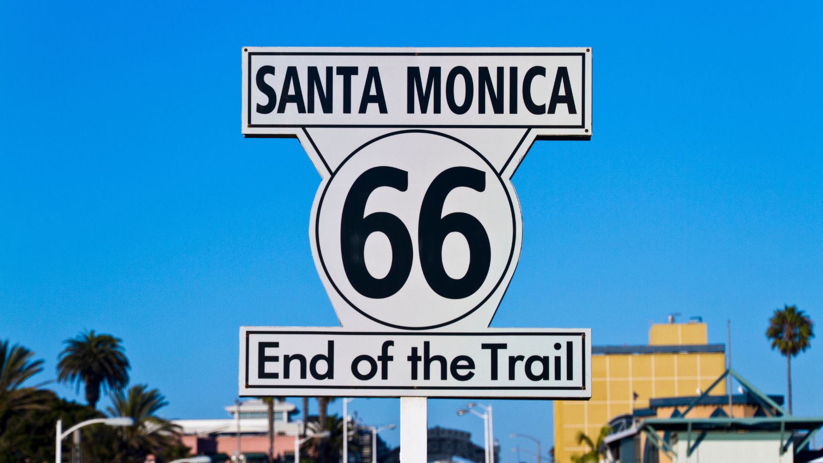 Route 66 sign in Santa Monica reading &ldquo;End of the Trail&rdquo; against a blue sky, marking the 100th anniversary of the historic route.