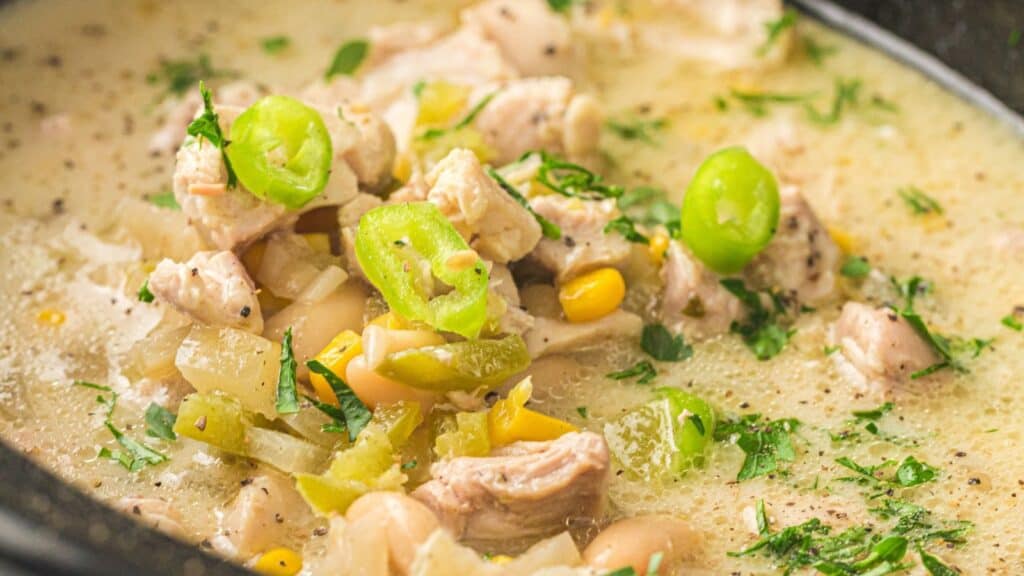 A close-up of chicken chili with white beans, corn, and sliced green peppers in a creamy broth.