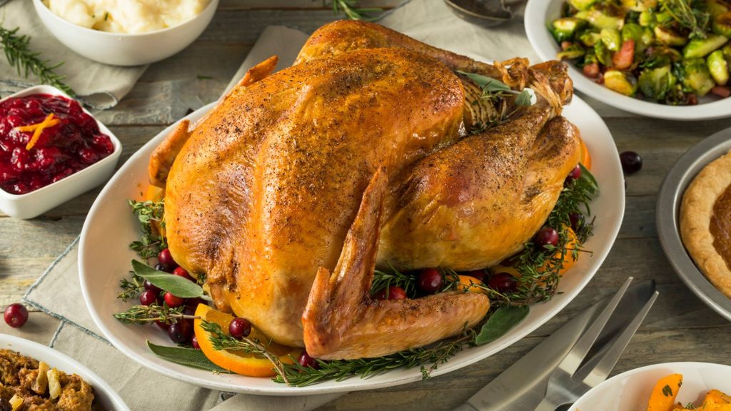 Roasted turkey garnished with herbs, orange slices, and cranberries on a serving platter, surrounded by side dishes.