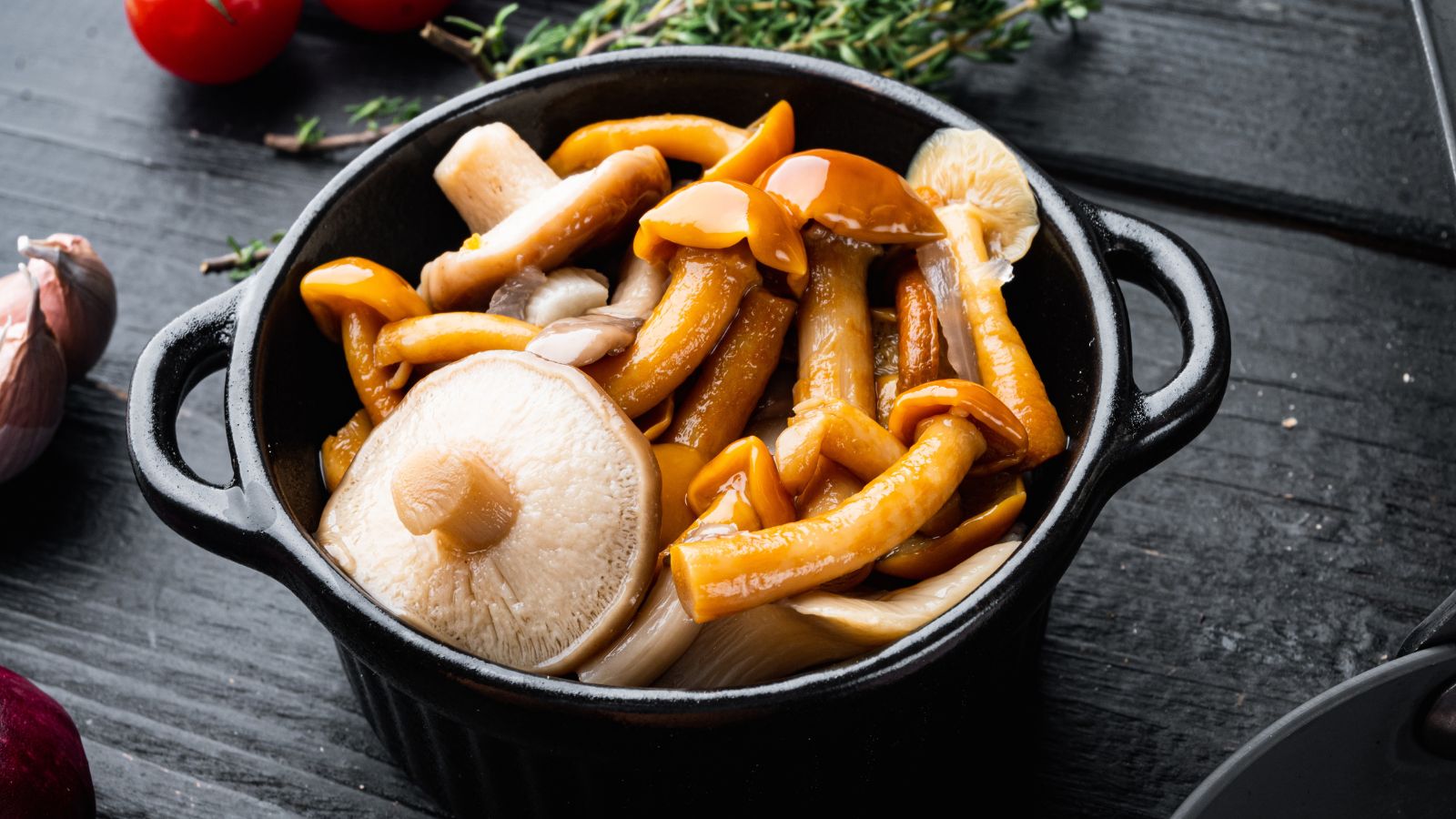 A black ceramic bowl filled with a variety of cooked wild mushrooms.